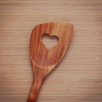 Wooden cooking utensils border. Wooden spatula with heart shape hole on bamboo cutting board with flat lay and copy space.