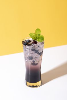 Cold and refreshing  blueberry punch cocktail with mint on yellow background. summer drink