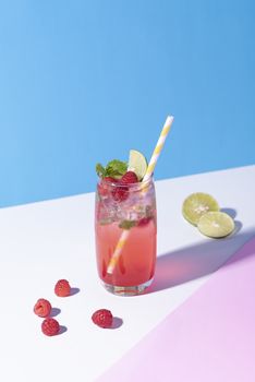 iced red raspberry punch cocktail with lime in glass on color background. summer drink.