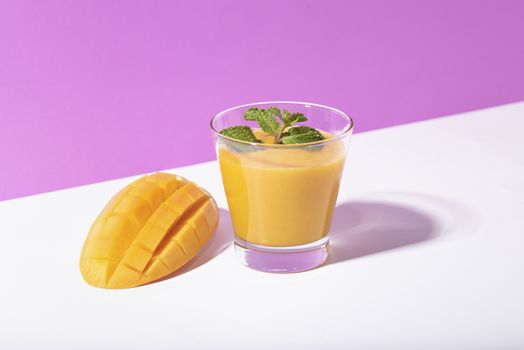 Fresh mango smoothie and ripe mango slice on purple background. summer drink.