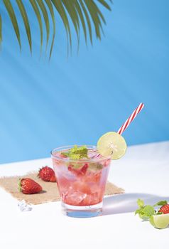 iced strawberry punch cocktail in glass with lemon on blue background. summer drink.