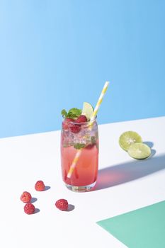 iced red raspberry punch cocktail with lime in glass on color background. summer drink.