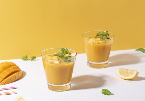 Fresh mango smoothie and ripe mango slice on color background. summer drink.