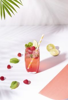 iced red raspberry punch cocktail with lime in glass on color background. summer drink.