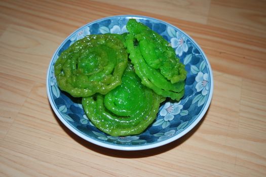 Crispy sweet Asian dessert green Jalebi cooked and served in ceramic plate, Indian sweet street food with juicy syrup, a closeup view.