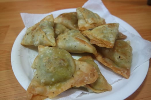 Closeup of delicious home made spicy and crunchy samosa pastries placed in a white ceramic plate on wooden floor