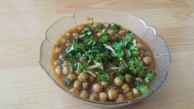 Home made dish served in glass bowl garnished with sliced onion and green coriander leaf and placed over wooden floor .Traditional lentils Channa Masala or chickpeas curry or chole bhature.