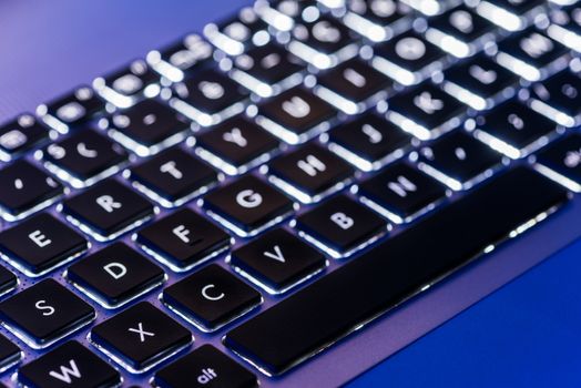 Backlit laptop keyboard close-up with selective focus in a blue ambiant light