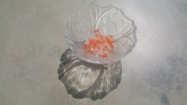 Shining, transparent, orange color crystal beads or gemstones or amber beads in a glass bowl over grey floor