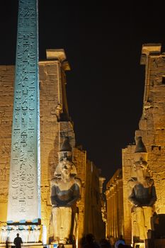 Large statue and obelisk at entrance pylon to ancient egyptian Luxor Temple lit up during night
