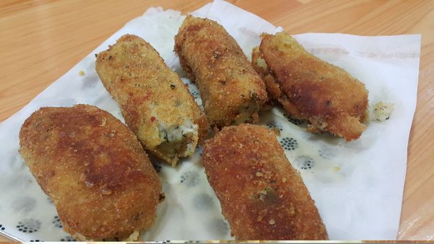 Closeup perspective view of home made spicy and delicious croquettes served in ceramic plate over wooden floor