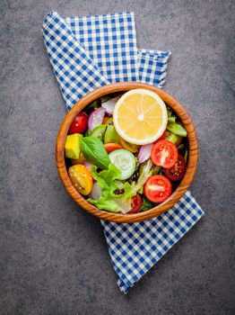 The bowl of healthy vegan salad . Various vegetables avocado, tomato, cucumber, red cabbage, basil and onion on dark stone background .