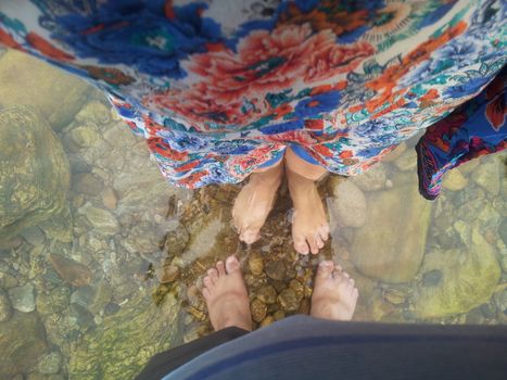 Top view of transparent water surface with human feet visible in it. Copy space for background and texture. Transparent water texture with view of stones under water.