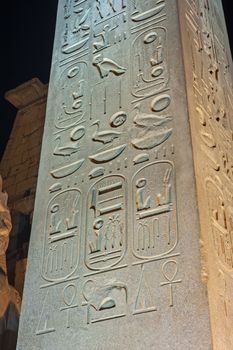 Large obelisk with hieroglyphic carvings at ancient egyptian Luxor Temple lit up during night