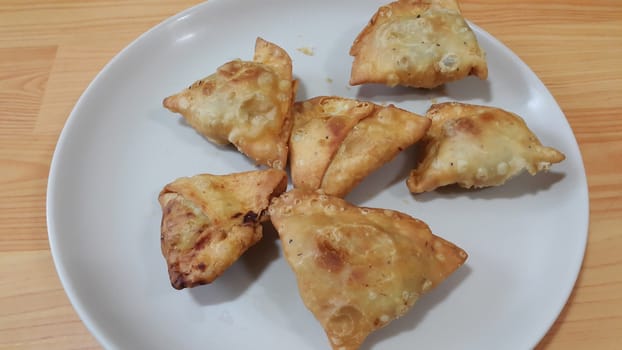 Closeup of delicious home made spicy and crunchy samosa pastries placed in a white ceramic plate on wooden floor