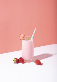 Strawberry smoothie in glass with straw and scattered berries on pink background.
