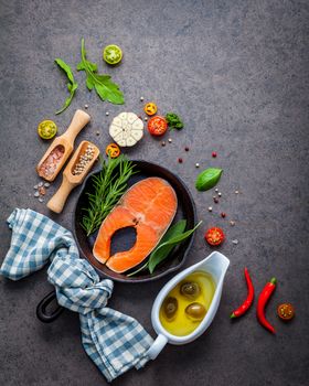 Salmon filet in old cast iron skille on dark stone background. Ingredients for making steak concept with copy space . Various herbs and seasoning rosemary ,sage leaves ,basil ,garlic and peppercorn.