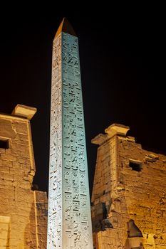 Large obelisk at entrance pylon to ancient egyptian Luxor Temple lit up during night