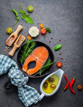 Salmon filet in old cast iron skille on dark stone background. Ingredients for making steak concept with copy space . Various herbs and seasoning rosemary ,sage leaves ,basil ,garlic and peppercorn.