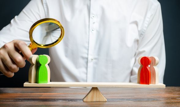 A man with a magnifying glass is looking at the rival red and green figures groups on scales. conflict resolution and the search for a compromise in the dispute. Research argument of each side