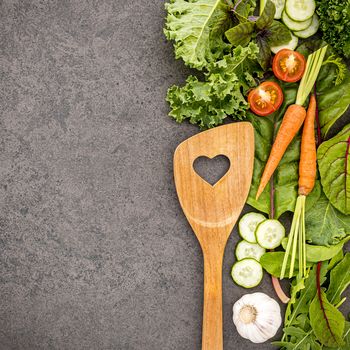 Wooden spoon and vegetables on dark stone background. Healthy food and cooking concept.