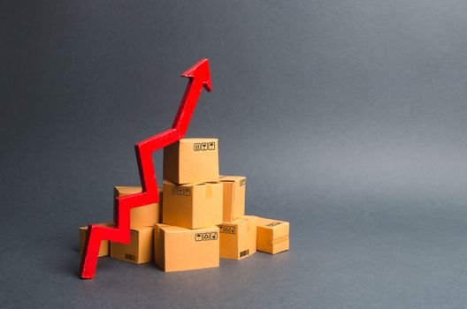 A pile of cardboard boxes and a red up arrow. The growth rate of production of goods and products, increasing economic indicators. Increasing consumer demand, increasing exports, imports. sales rise