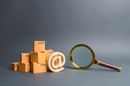 Pile of boxes with email symbol AT and a magnifying glass. Concept search for goods and services. Search for customers for sale, sales and retail. Tracking parcels via the Internet. Quality control