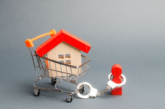 A person is handcuffed to a house on a supermarket cart. The concept of a large debt on a loan or mortgage. Financial dependence, unavailable housing for young families. Freeze of property.