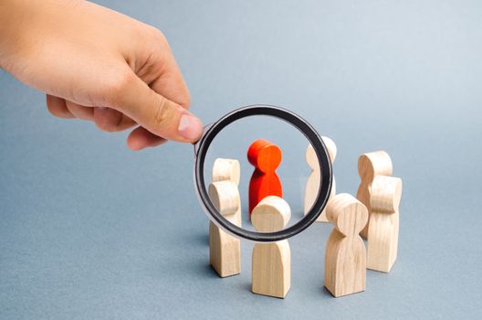 Magnifying glass is looking at the People stand in a circle on a gray background. Communication. Business team, teamwork, team spirit. Wooden figures of people. A circle of people. Selective focus