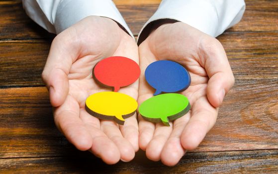 Man holds multicolored speech bubbles in his hands. Listen to other opinions and points of view, accepting criticism and comments. Reverse contact with customers and buyers. Freedom of speech.