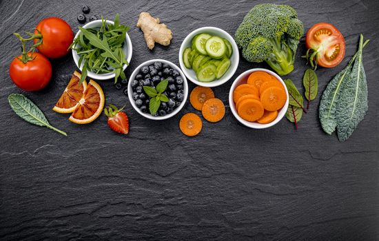 Colourful healthy smoothies and juices in bottles with fresh tropical fruit and superfoods on dark stone background with copy space.