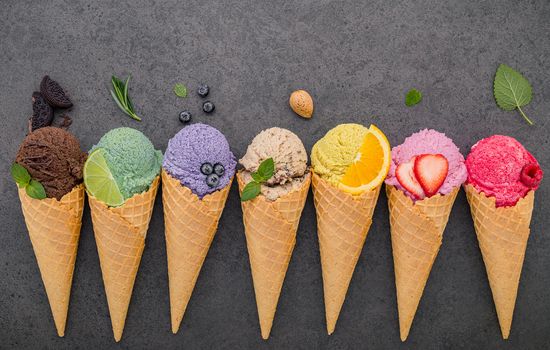 Various of ice cream flavor in cones blueberry ,lime ,pistachio ,almond ,orange ,chocolate ,vanilla and coffee set up on dark stone background . Summer and Sweet menu concept.