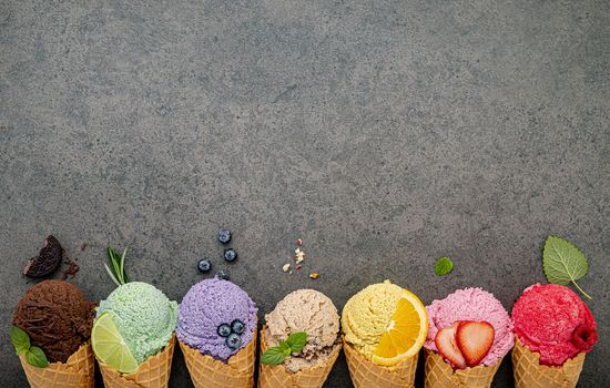 Various of ice cream flavor in cones blueberry ,lime ,pistachio ,almond ,orange ,chocolate ,vanilla and coffee set up on dark stone background . Summer and Sweet menu concept.