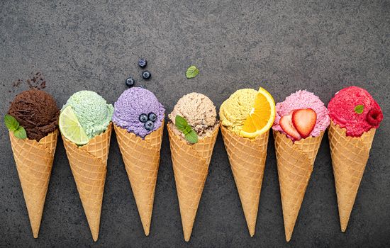 Various of ice cream flavor in cones blueberry ,lime ,pistachio ,almond ,orange ,chocolate ,vanilla and coffee set up on dark stone background . Summer and Sweet menu concept.