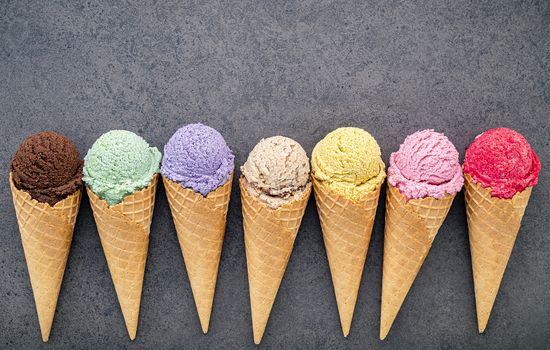 Various of ice cream flavor in cones blueberry ,lime ,pistachio ,almond ,orange ,chocolate ,vanilla and coffee set up on dark stone background . Summer and Sweet menu concept.