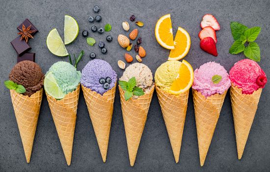 Various of ice cream flavor in cones blueberry ,lime ,pistachio ,almond ,orange ,chocolate ,vanilla and coffee set up on dark stone background . Summer and Sweet menu concept.