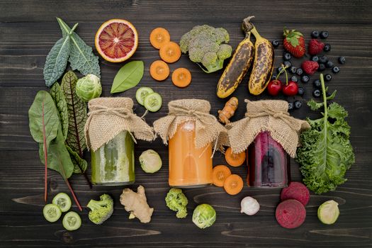 Colourful healthy smoothies and juices in bottles with fresh tropical fruit and superfoods on wooden background.