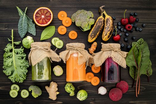 Colourful healthy smoothies and juices in bottles with fresh tropical fruit and superfoods on wooden background.