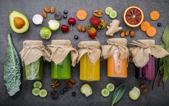 Colourful healthy smoothies and juices in bottles with fresh tropical fruit and superfoods on dark stone background with copy space.