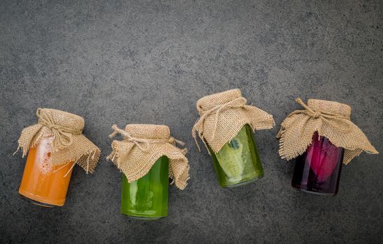 Colourful healthy smoothies and juices in bottles on dark stone background with copy space.