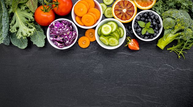 Colourful healthy smoothies and juices in bottles with fresh tropical fruit and superfoods on dark stone background with copy space.