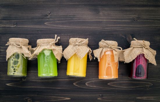 Colourful healthy smoothies and juices in bottles with fresh tropical fruit and superfoods on wooden background.