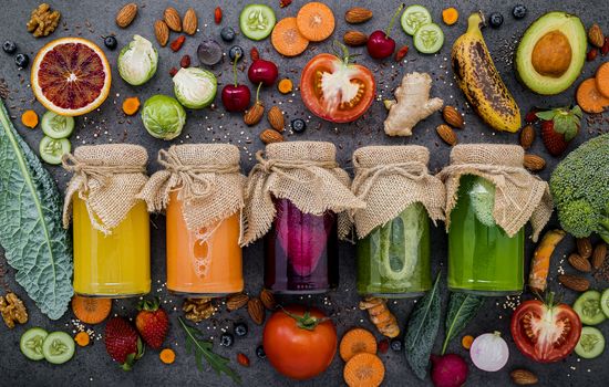 Colourful healthy smoothies and juices in bottles with fresh tropical fruit and superfoods on dark stone background with copy space.