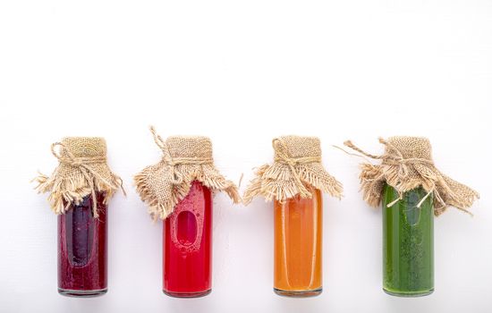 Colourful healthy smoothies and juices in bottles on white background with copy space.