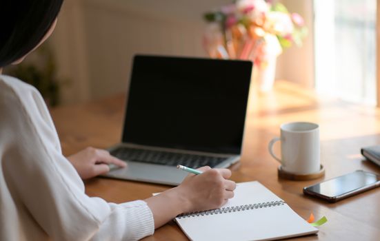 A young woman is using a laptop and writing a report. She works from home.