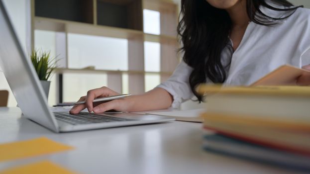 Close-up shot of Girl holding a pen in hand on a laptop keyboard. She is working in a modern office.