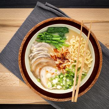 Asian ramen noodle pork bone based soup with pork chashu on cutting board background.