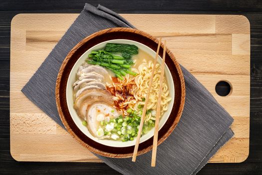 Asian ramen noodle pork bone based soup with pork chashu on cutting board background.