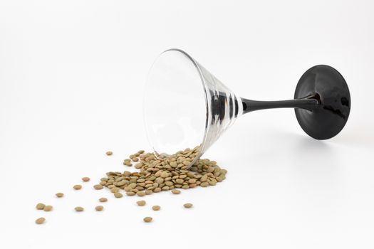 Natural organic dry lentils and glass fell on white background. Conceptual/abstract representation of the end of holidays. The end of the party. Back to the real life. NYE.