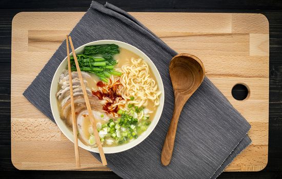 Asian ramen noodle pork bone based soup with pork chashu on cutting board background.